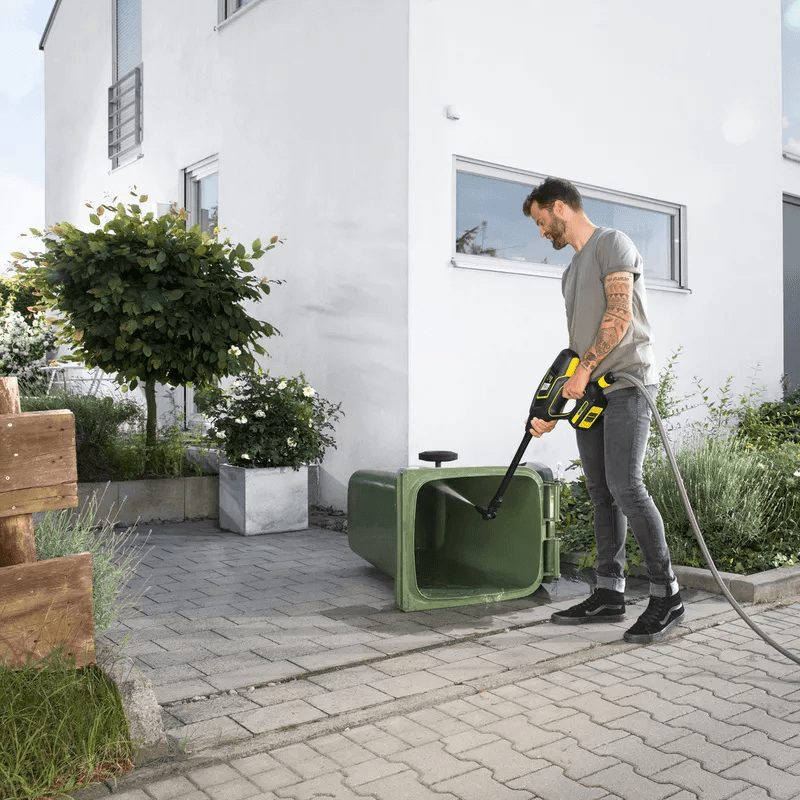 Operative cleaning a green wheelie bin with a portable pressure washer