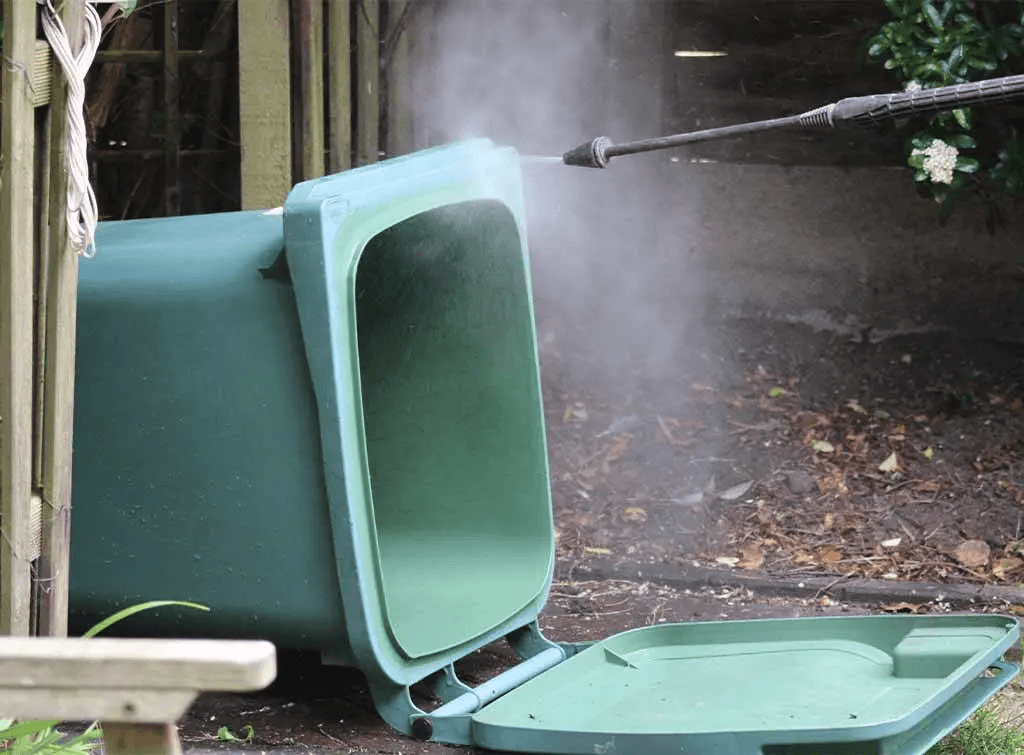 Green wheelie bin on its side being pressure-washed outdoors