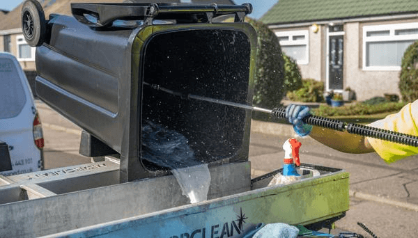 Wheelie bin tipped on cleaning equipment while being pressure-washed